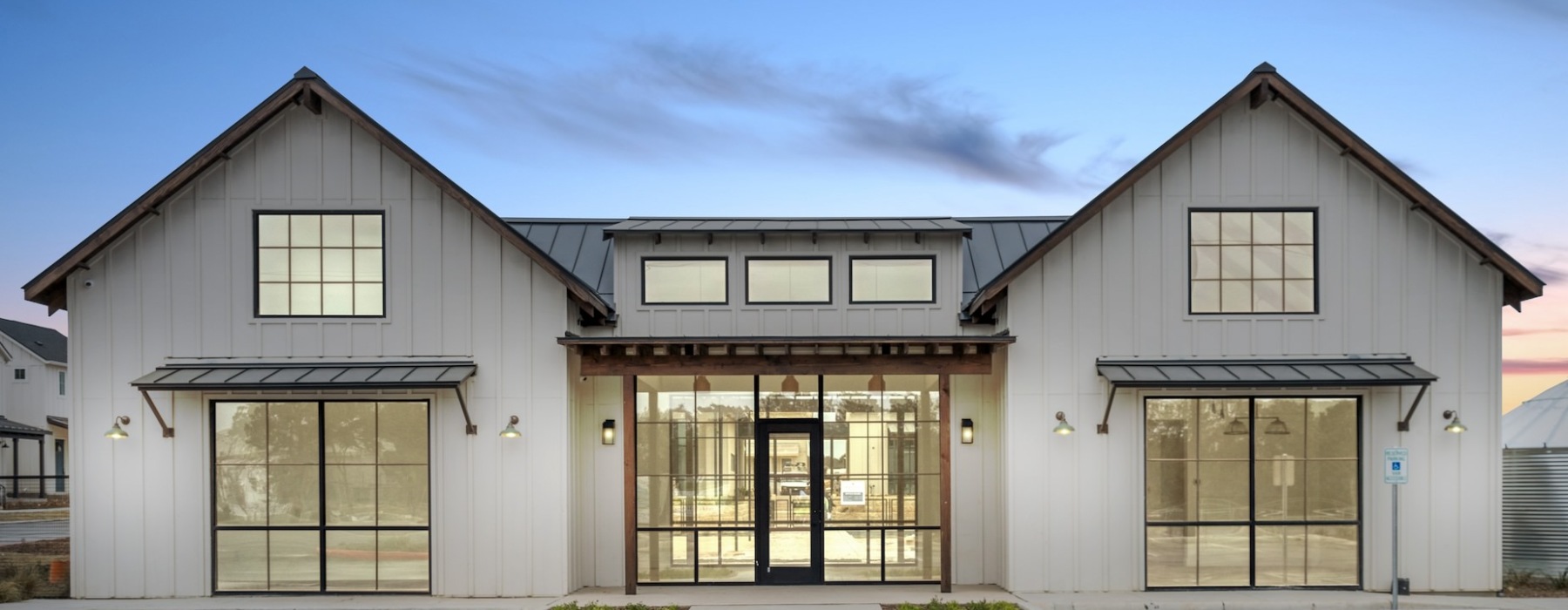 Front view of a white farmhouse-style apartment bathed in the evening light, set against a tranquil backdrop with vibrant sunset colors