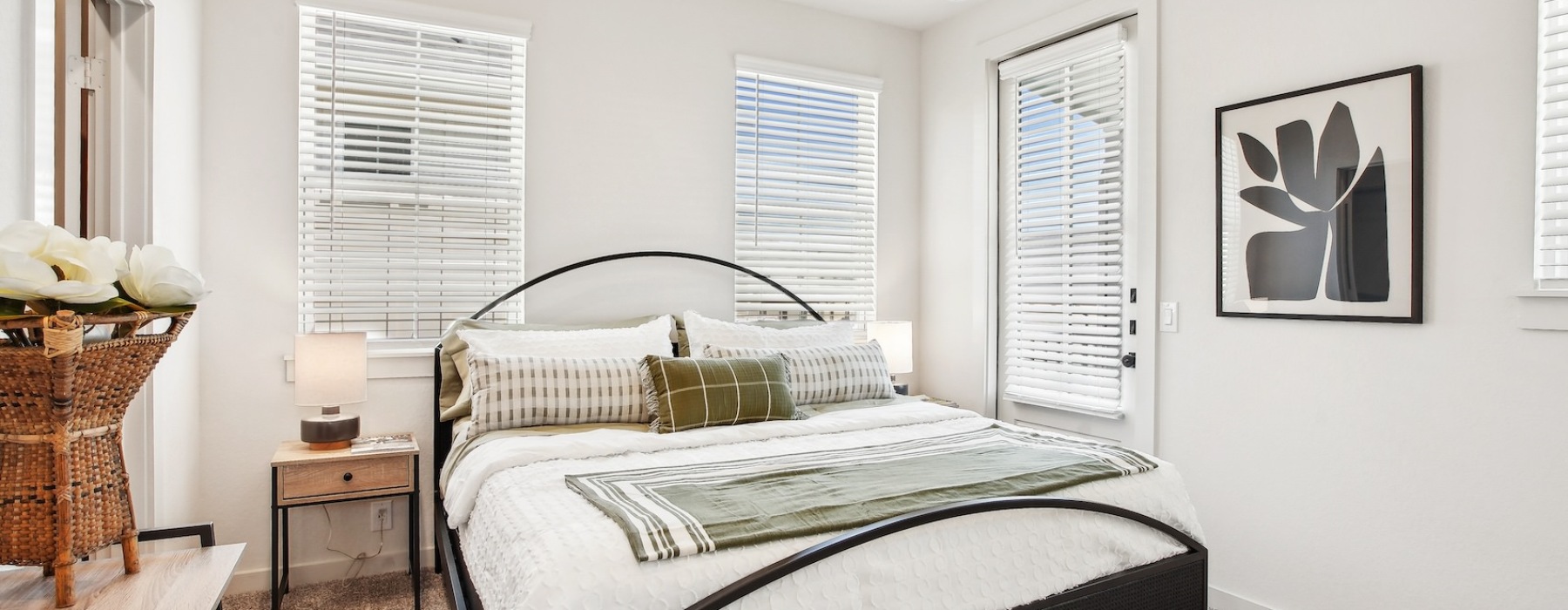 Charming bedroom featuring a fresh white and green bed with plush pillows, and expansive window blinds 