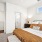 Bright bedroom featuring a white bed with crisp linens, a brown dresser, and a white door