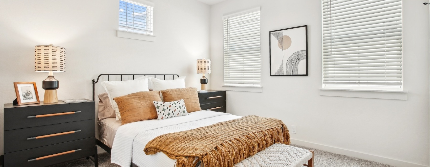 A cozy bedroom with a white bed, brown dresser, and a window blinds