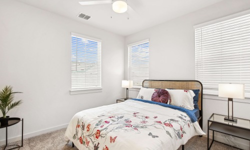 Bright primary bedroom in Two Bedroom townhomes San Antonio featuring large windows, modern furnishings, and abundant natural light.