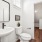 A minimalist bathroom with a white sink and toilet, highlighted by a stylish mirror and adorned with pale, soothing wall colors